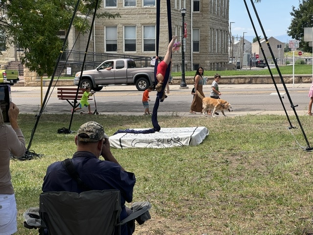 Aerial artist holding an inverted split on blue silks above the Walsenburg Farm and Makers Market in downtown Walsenburg